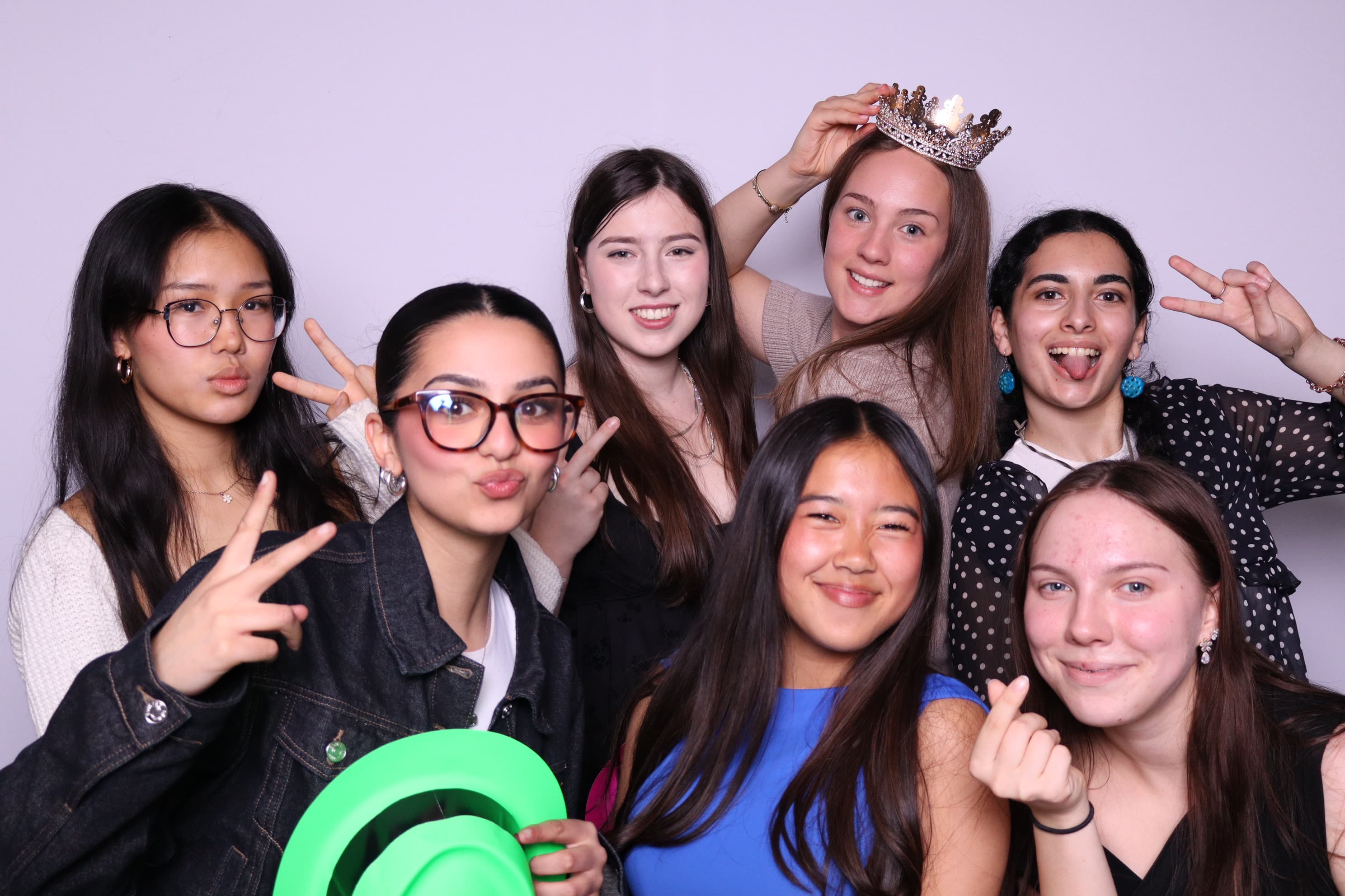Seven friends posing with crown and balloon props at photo booth